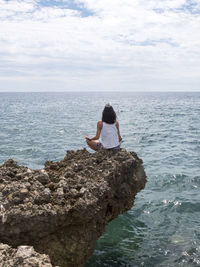 Rear view of woman meditation on rock against sea