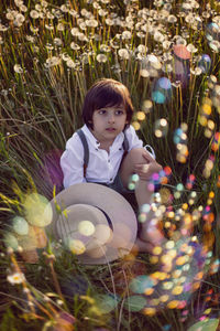 Funny happy a beautiful boy child sit in hat on field with white dandelions. soap bubbles are flying
