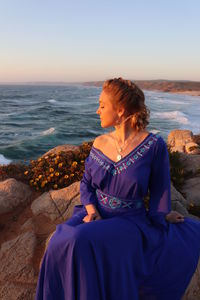 Woman sitting on rock looking at sea against sky