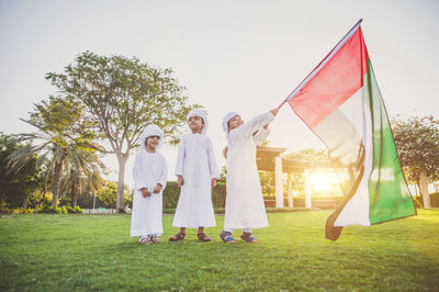 Children holding flag while standing on grassland against trees