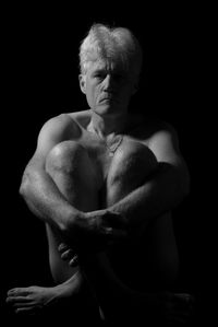 Naked mature adult man  sitting over black background