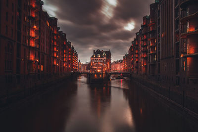 Canal amidst illuminated buildings against sky at dusk