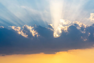 Low angle view of sunlight streaming through clouds