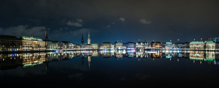 Illuminated buildings by river against sky at night