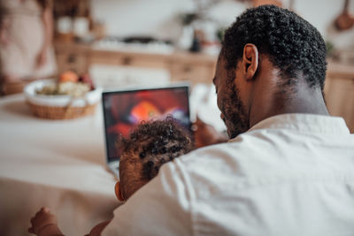 Rear view of man using mobile phone at home