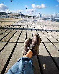 Low section of woman sitting on boardwalk during sunny day