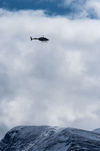 Low angle view of helicopter flying over snowcapped mountain