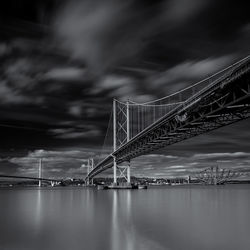 Low angle view of bridge over river against cloudy sky