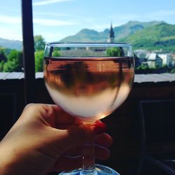 Close-up of hand holding wineglass against sky