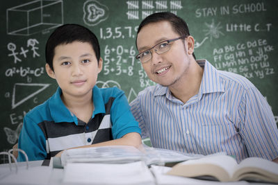 Boy with teacher at table against blackboard