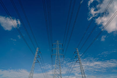 Low angle view of electricity pylon against blue sky