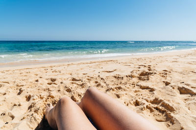 Low section of legs on beach against clear sky