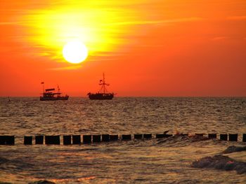 Silhouette boats sailing on sea against orange sky