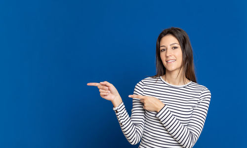 Portrait of smiling young woman pointing against blue background