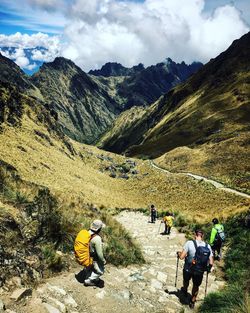 People walking on mountain road against cloudy sky