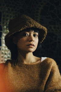 Portrait of young woman wearing brown hood at illuminated restaurant