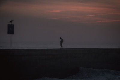 Silhouette man standing by sea against sky during sunset