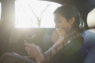 Young asian businesswoman looking at smartphone sitting in car service limousine