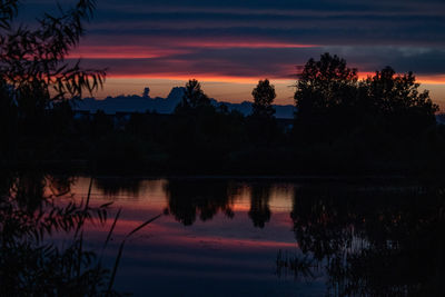 Silhouette trees by lake against romantic sky at sunset