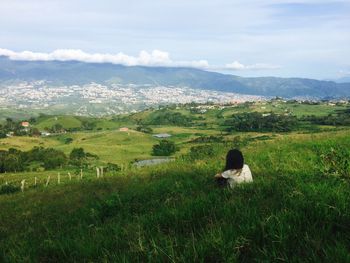 Rear view of woman sitting on field against sky