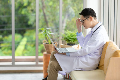 Young man using smart phone while sitting on laptop