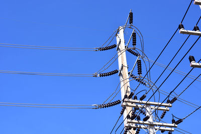 Low angle view of electricity pylon against blue sky