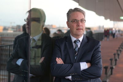 Portrait of businessman with arms crossed leaning on glass outdoors