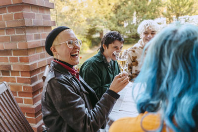 Side view of happy gay woman laughing while holding wineglass during dinner party in back yard