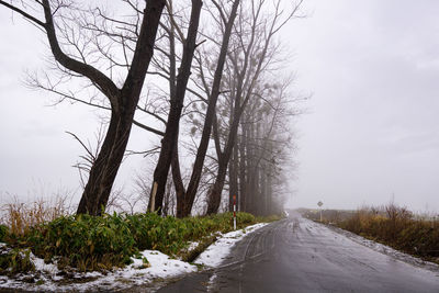 Road amidst bare trees against sky during winter