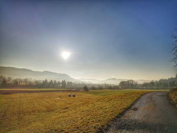 Dirt road amidst field against sky