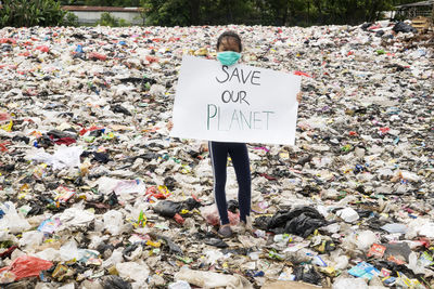 Portrait of girl holding text on placard at landfill 