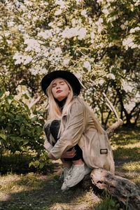 Portrait of woman wearing hat standing by tree