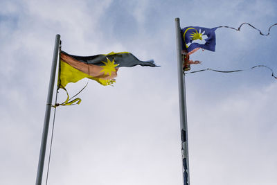 Low angle view of torn and worn out flags of sarawak and malaysia against sky.