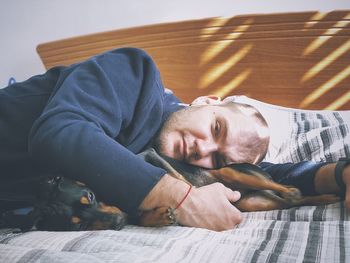 Portrait of man lying with dog on bed at home