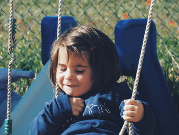 Close-up of cute girl sitting on swing at playground