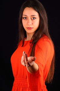 Portrait of beautiful young woman gesturing while standing against black background