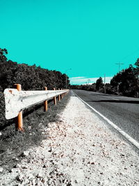 Empty road by trees against clear sky