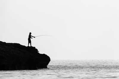 Man standing on rock fishing against clear sky