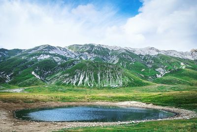 Scenic view of pond in front of green mountains against sky