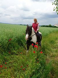 Woman sitting on horse at field against sky