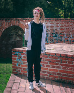 Full length of young woman standing against brick wall