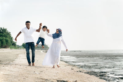 Happy family standing on shore at beach against sky