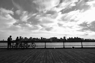 People riding bicycle on bridge over river against sky