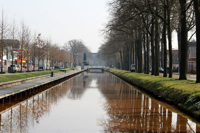 Canal amidst bare trees against sky