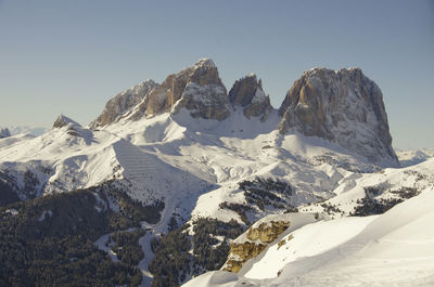 Huge rocks of dolomite mountains, rising above the snow, with a snowy valley and trees below