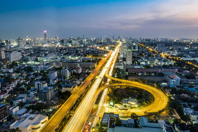 High angle view of light trails on roads in illuminated city during sunset