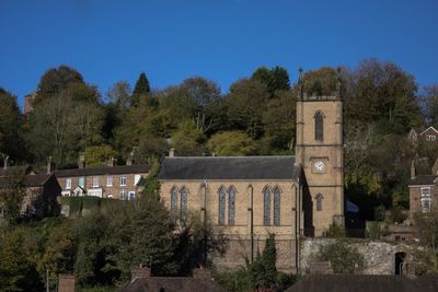 Trees and plants against building against clear blue sky