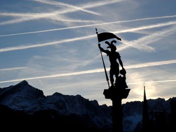 Low angle view of silhouette sculpture against cloudy sky