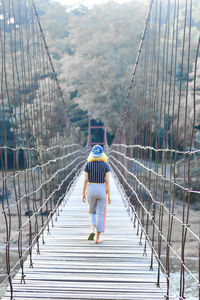 Rear view of woman walking on footbridge in forest