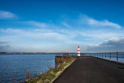 Lighthouse amidst sea and buildings against sky